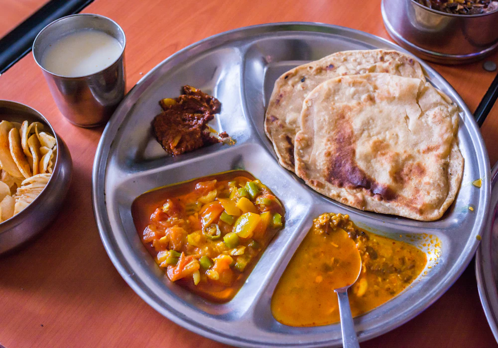 A homestyle Indian thali in a steel plate with dal, sabzi, curry and fresh roti
